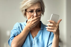 Closeup older woman looks at smartphone screen with distressed expression